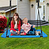 Kids sitting on blue platform tree swing in front of a house. 